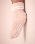 Baby with a medium skin tone wearing a blush baby crew sock with white heart and dot silicone grips on a blush background