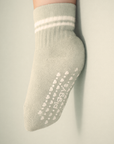 Baby with a light skin tone wearing a sage baby crew sock with white heart and dot silicone grips on a sage background