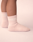 Baby with a medium skin tone wearing a pair of blush baby crew socks with white silicone grips on a blush background