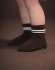 Baby with a light skin tone wearing a pair of dark brown baby crew socks with white silicone grips on an espresso brown background