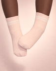Baby with a dark skin tone wearing a pair of blush baby crew socks on a blush background.