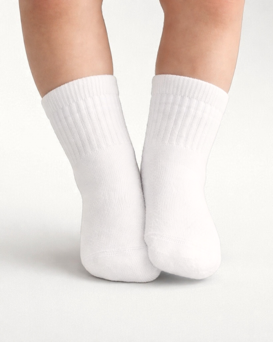 Baby with a light skin tone wearing a pair of white baby crew socks on an off-white background.