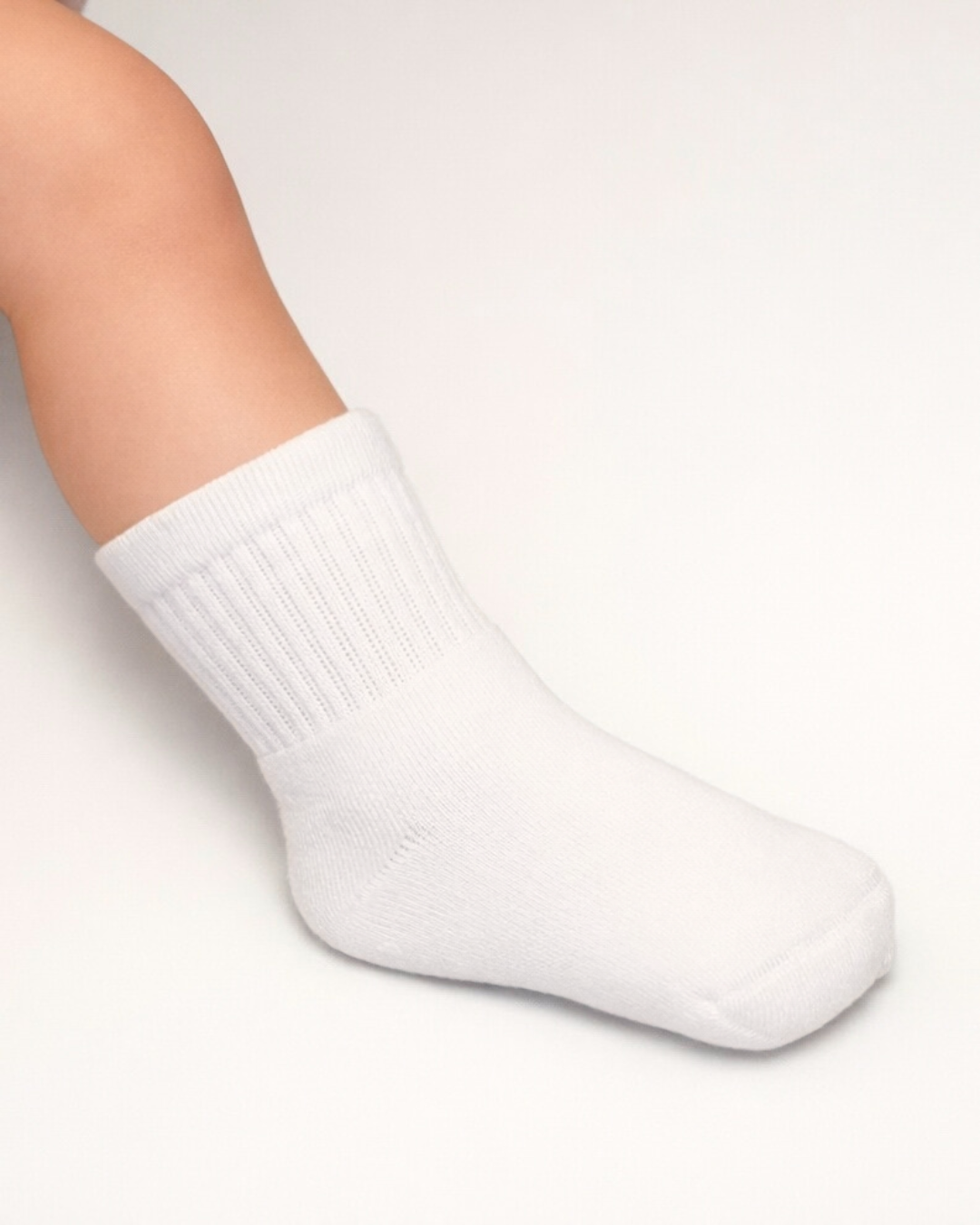 Baby with a light skin tone wearing a pair of white baby crew socks on an off-white background.