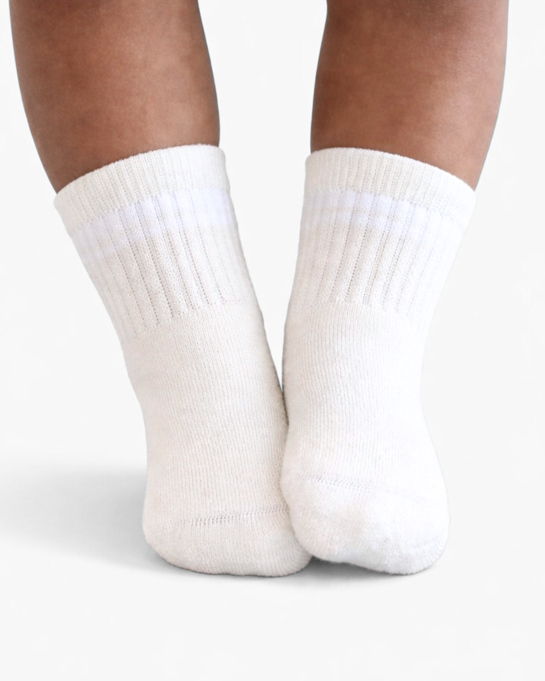 Pair of white baby crew socks with  silicone grips on an off-white background