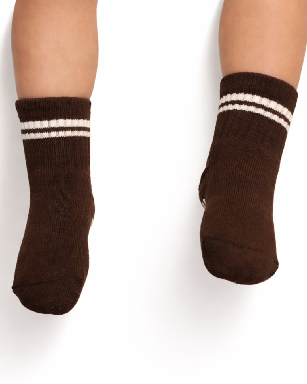 Pair of dark brown baby crew socks with white stripes and silicone grips on an off-white background