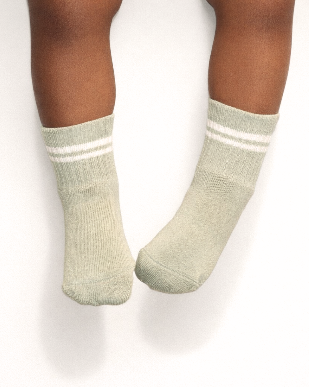 Pair of light sage baby crew socks with silicone grips on an off-white background