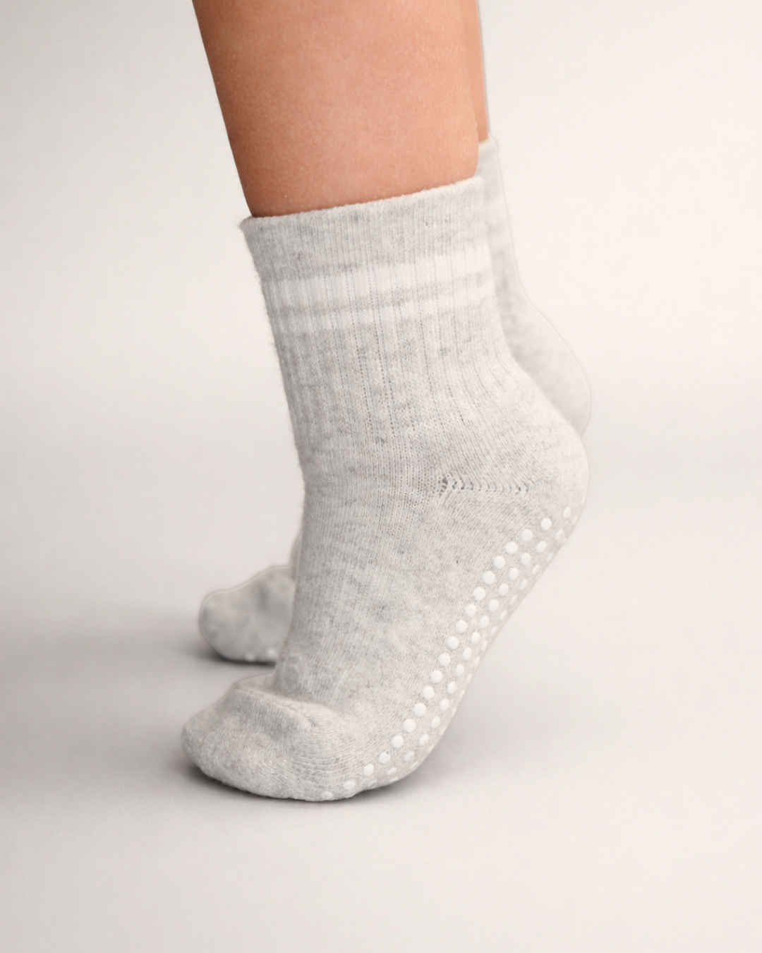 Toddler with a light skin tone wearing a pair of heather grey toddler crew socks on a grey background.