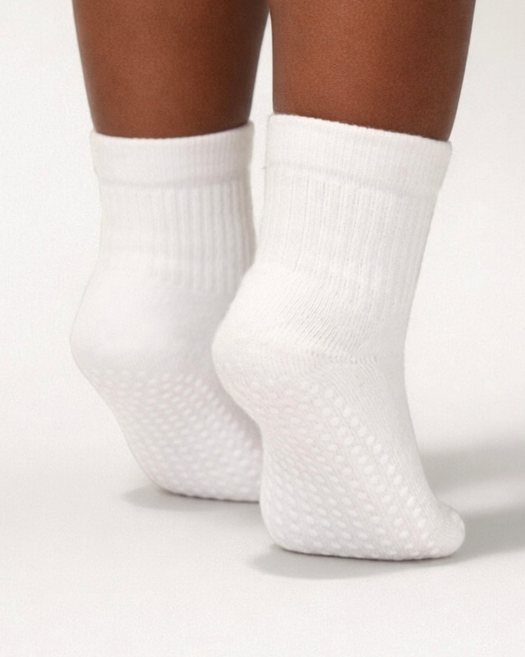 White toddler crew sock with white dot silicone grips on an off-white background.