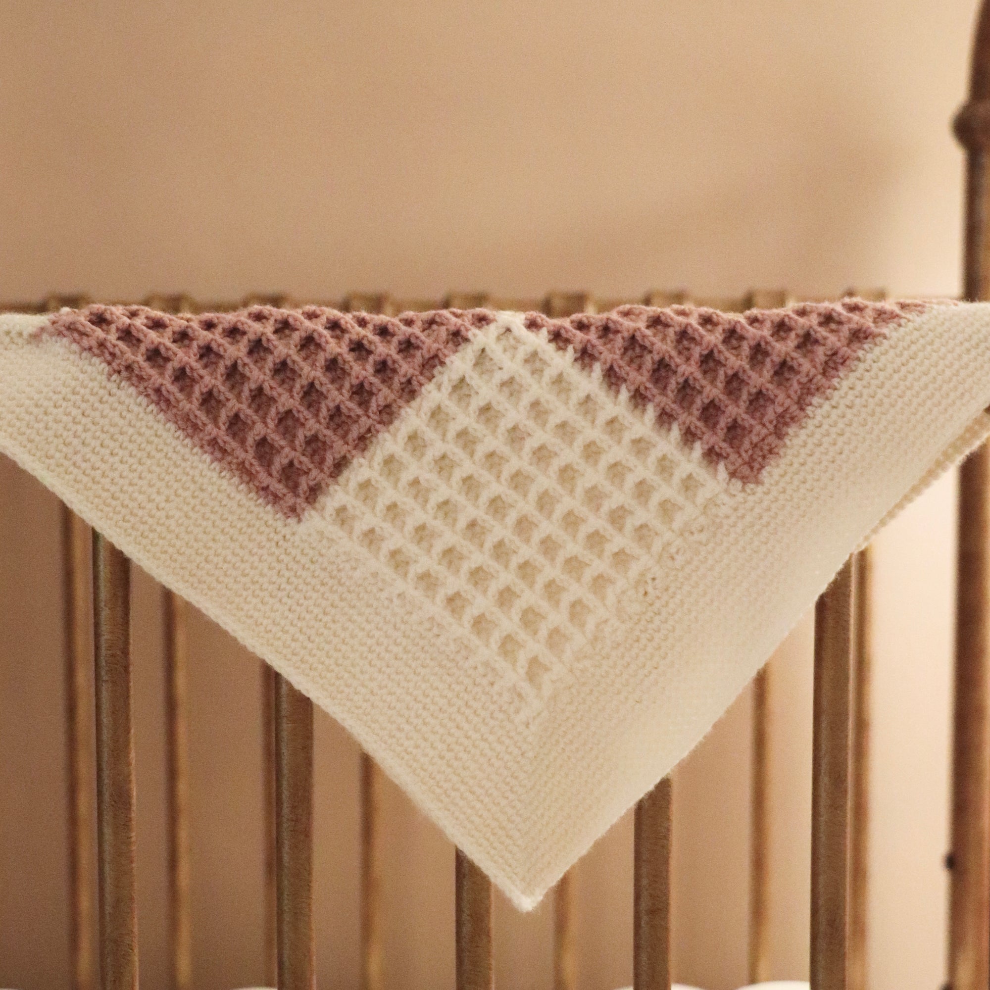 merino wool checkered waffle knit baby lovey blanket in dusty rose and bone draped over a crib