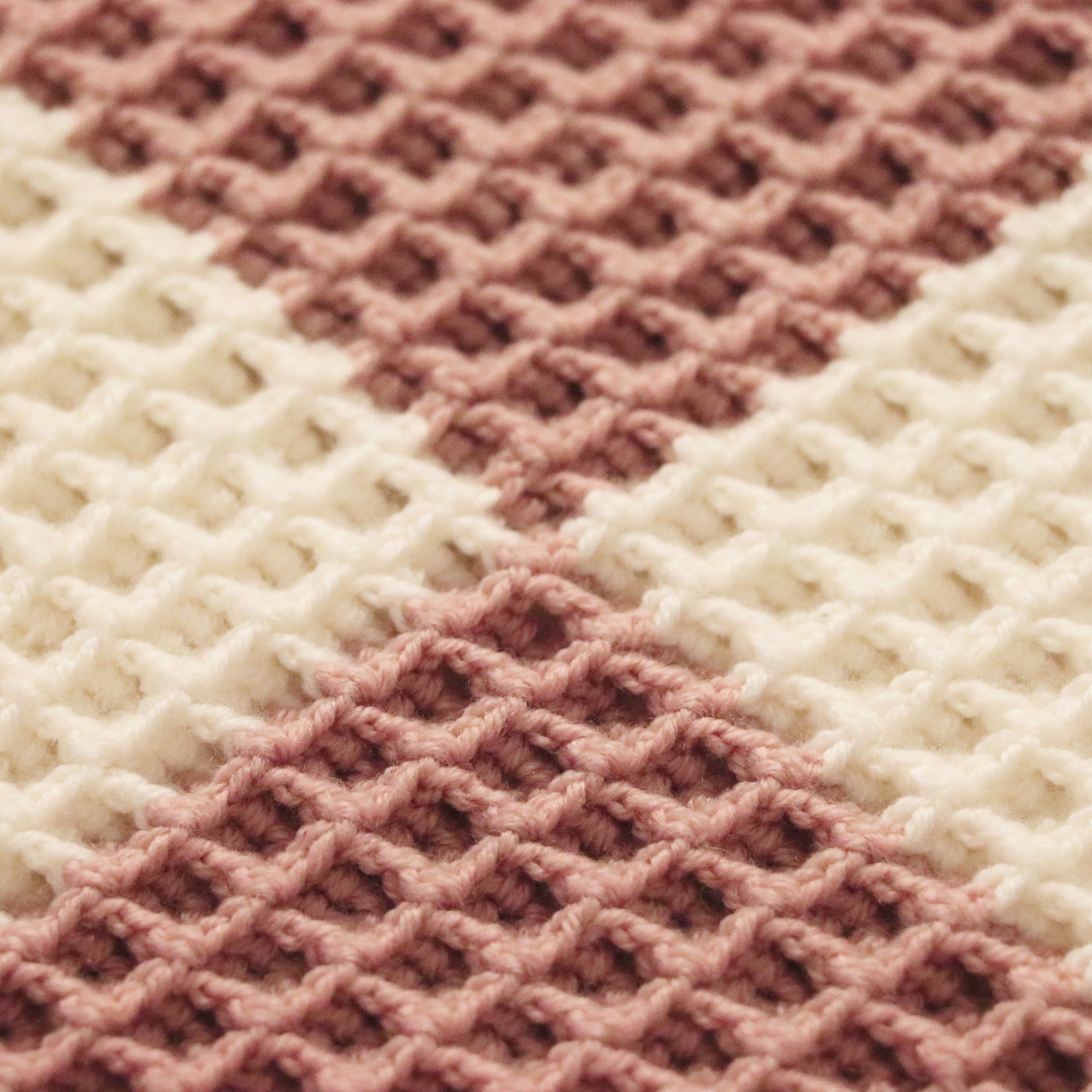 close-up of a merino wool checkered waffle knit baby lovey blanket in dusty rose and bone