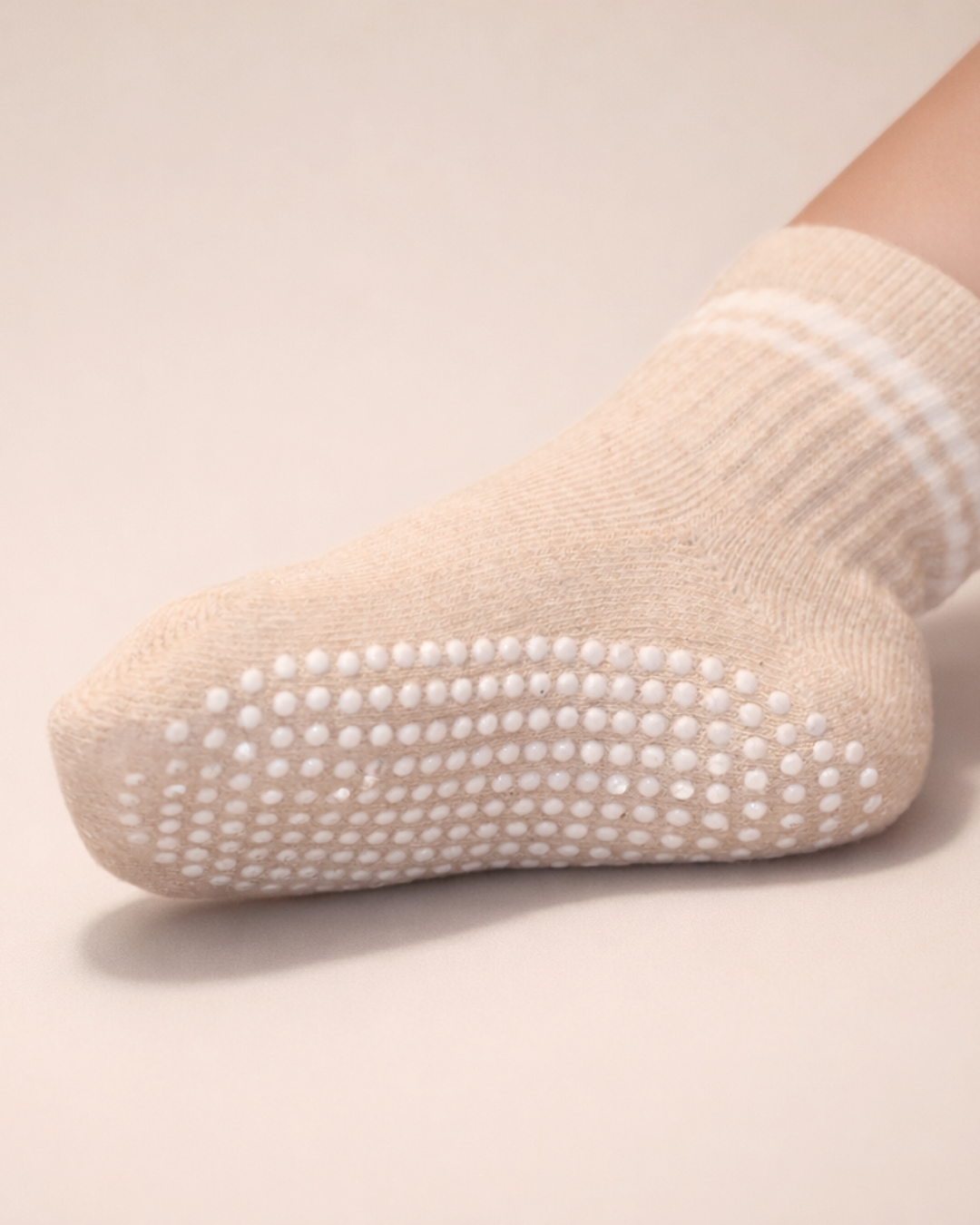 Heather beige toddler crew sock with white dot silicone grips on a beige background.