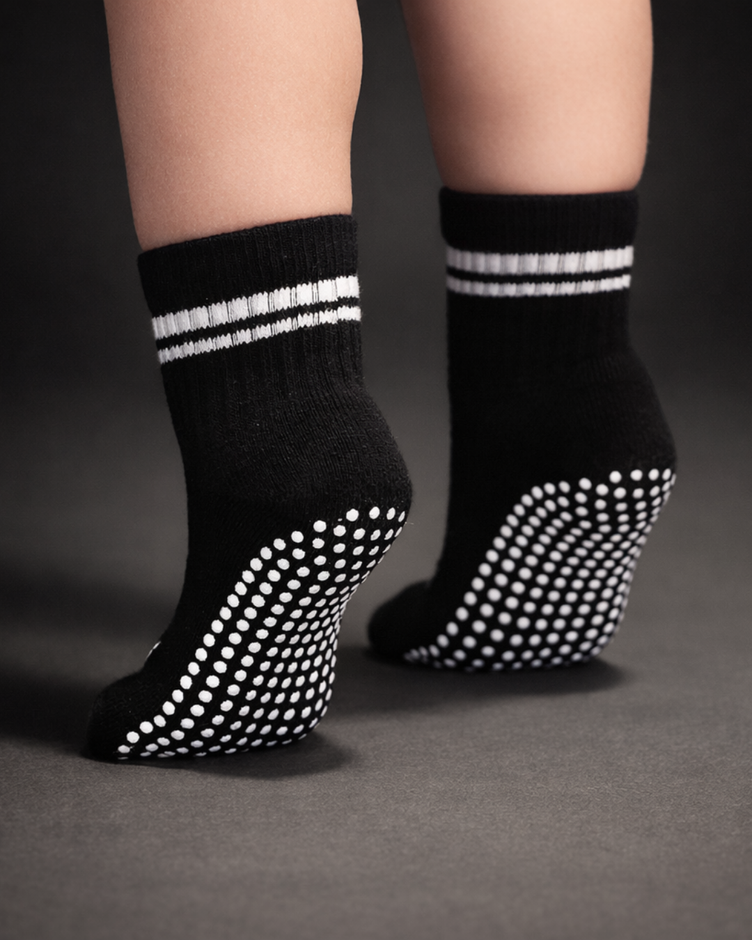 Black toddler crew sock with white dot silicone grips on a dark grey background.