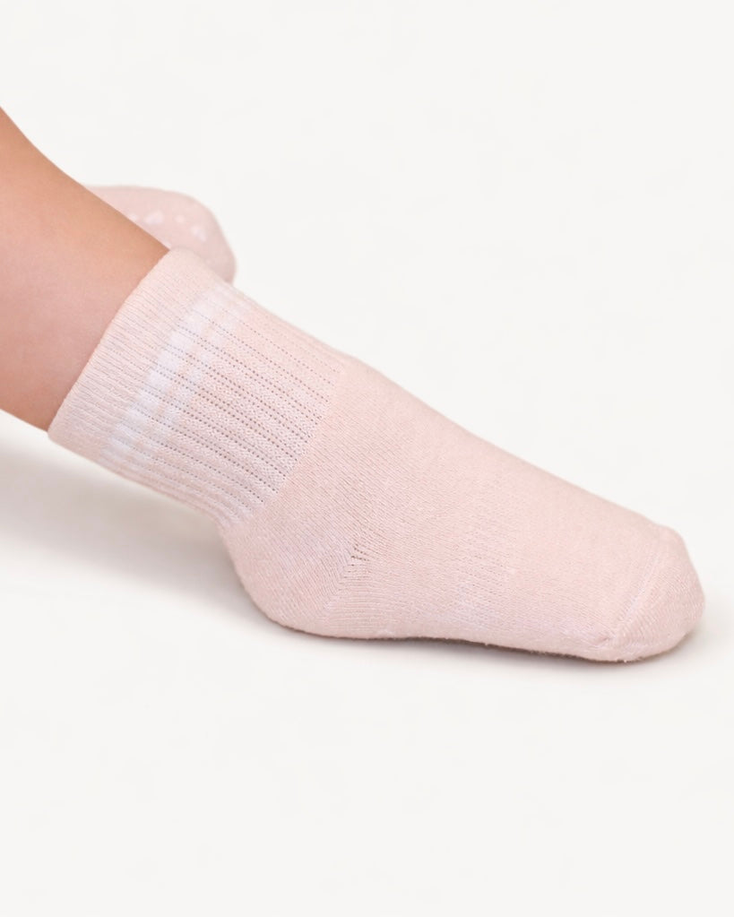 Pair of white baby crew socks with silicone grips on an off-white background