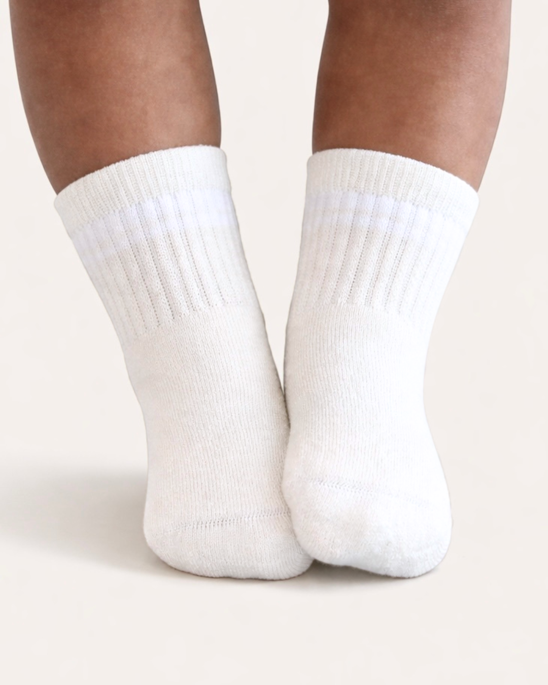 Pair of white baby crew socks with silicone grips on an off-white background