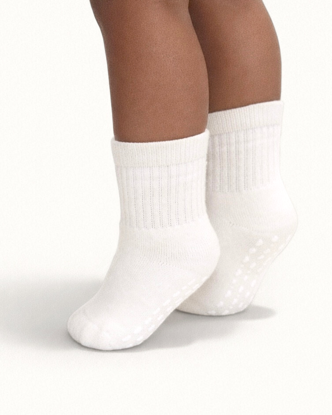 Pair of white baby crew socks with silicone grips on an off-white background