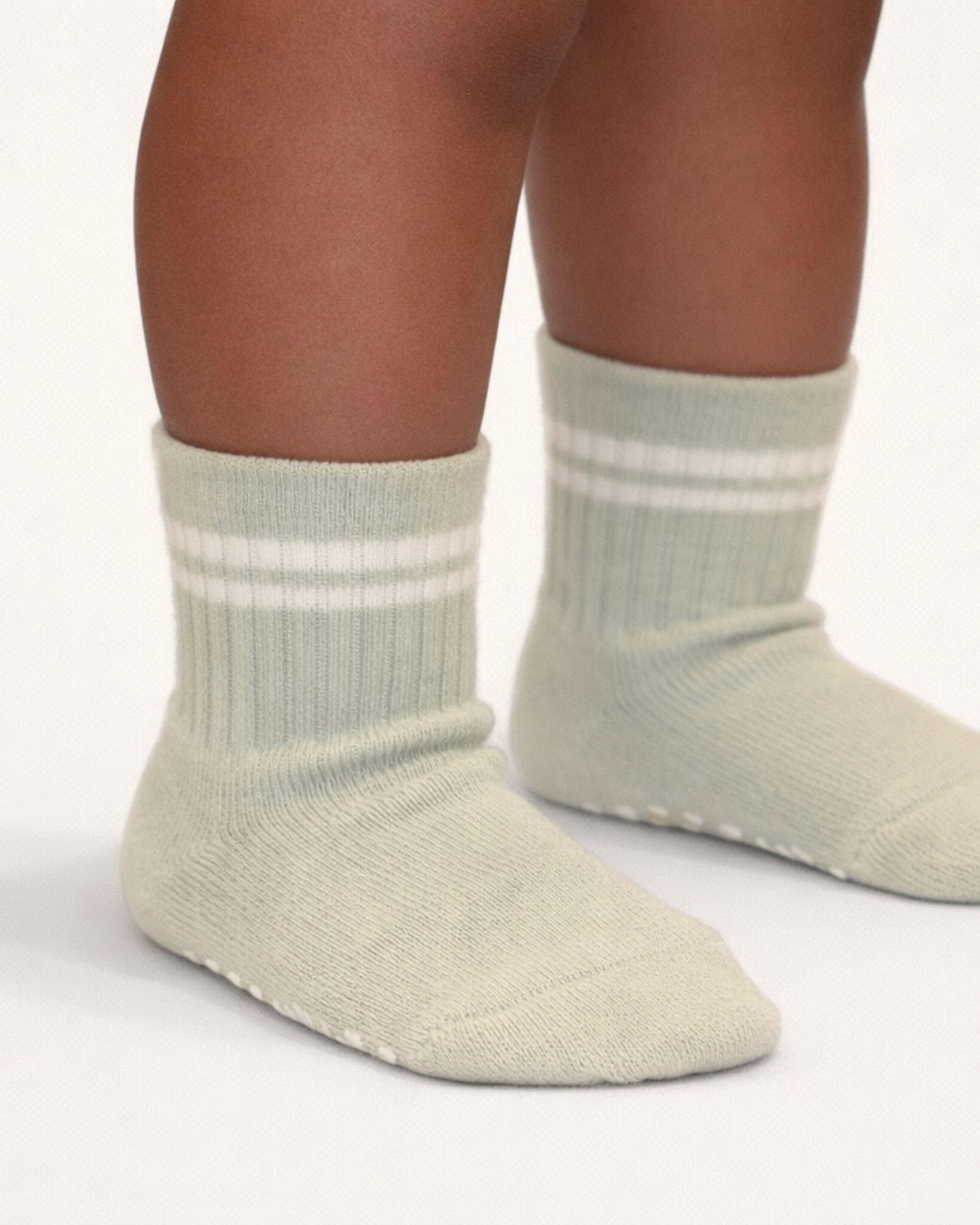 Pair of light sage baby crew socks with silicone grips on an off-white background