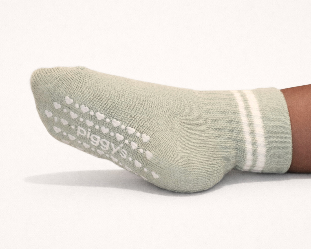 Light sage baby crew sock with heart patterned Piggy's grips on a white background