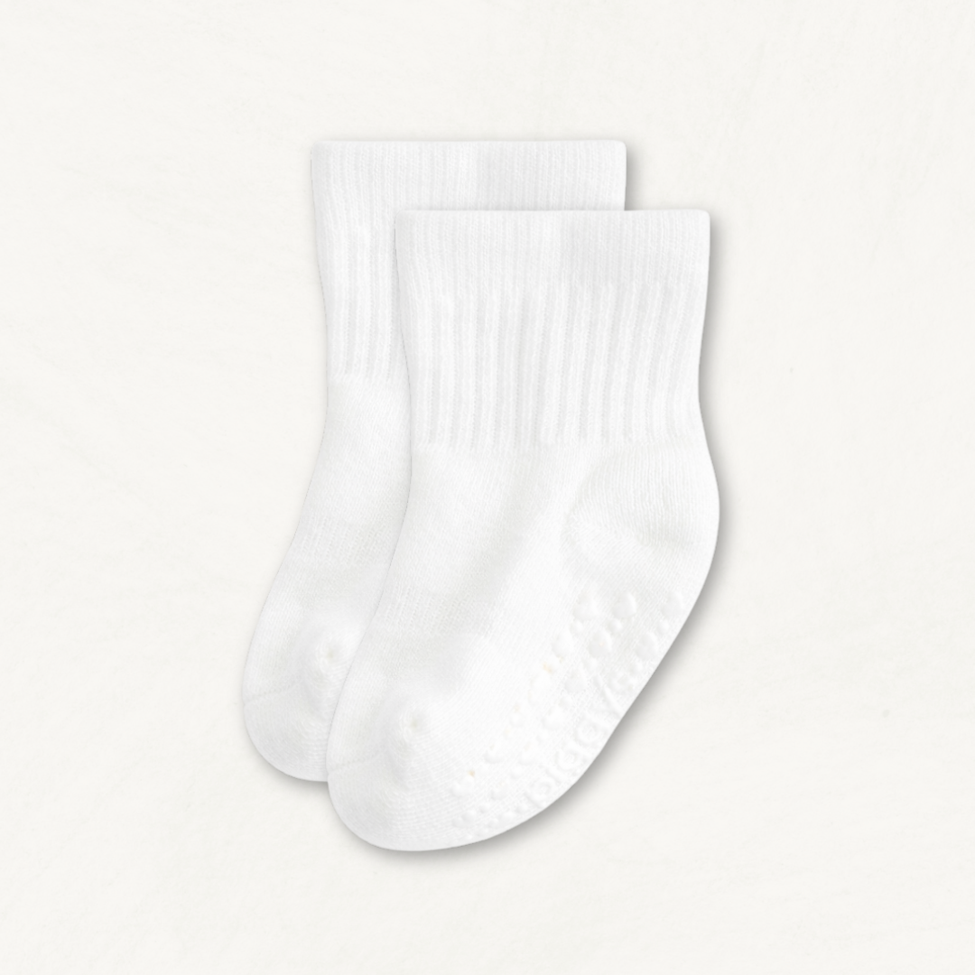 Pair of white baby crew socks with heart pattern silicone grips on an off-white background