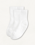 Pair of white baby crew socks with heart pattern silicone grips on an off-white background
