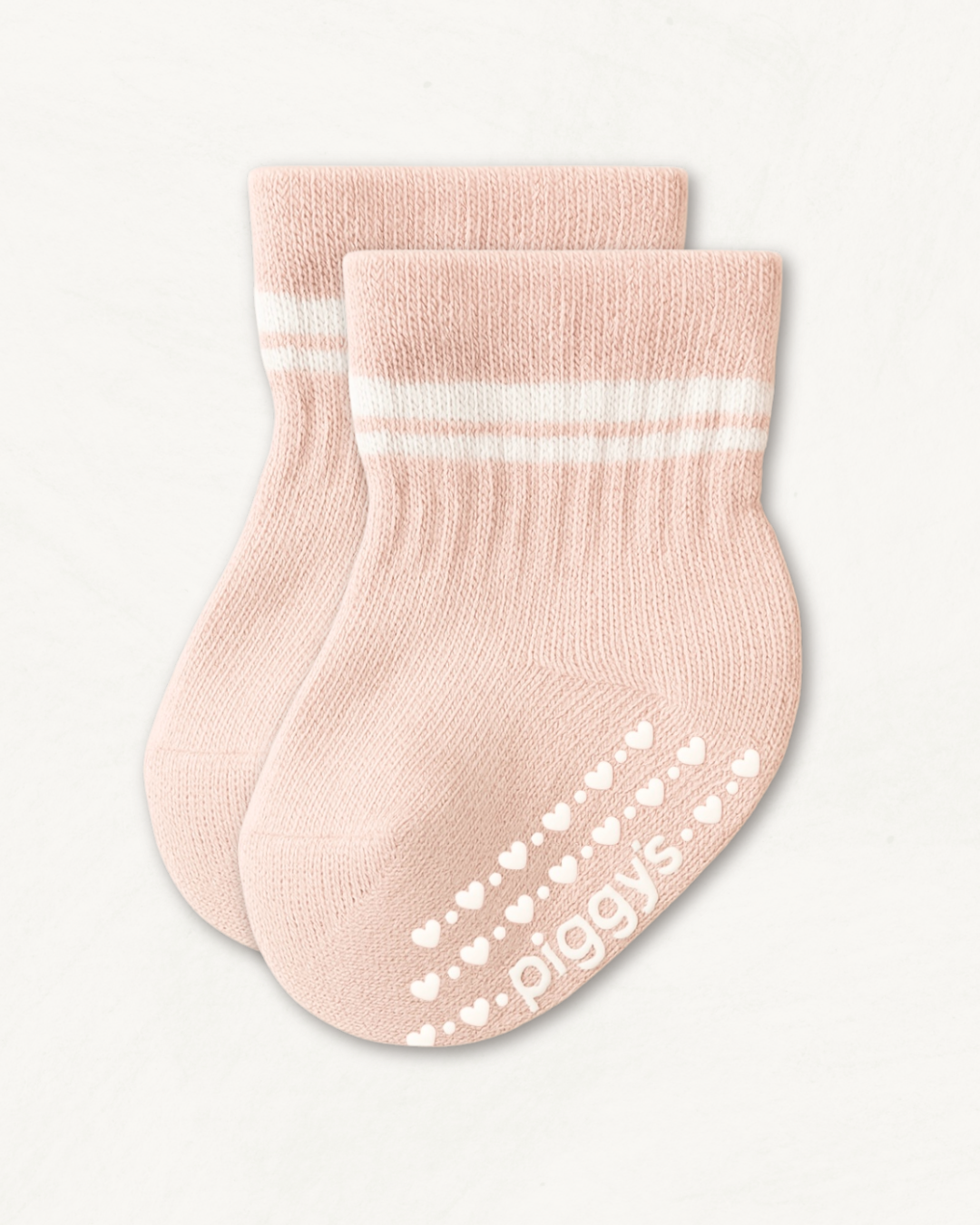 Pair of blush pink crew socks with white stripes and heart pattern silicone grips on an off-white background