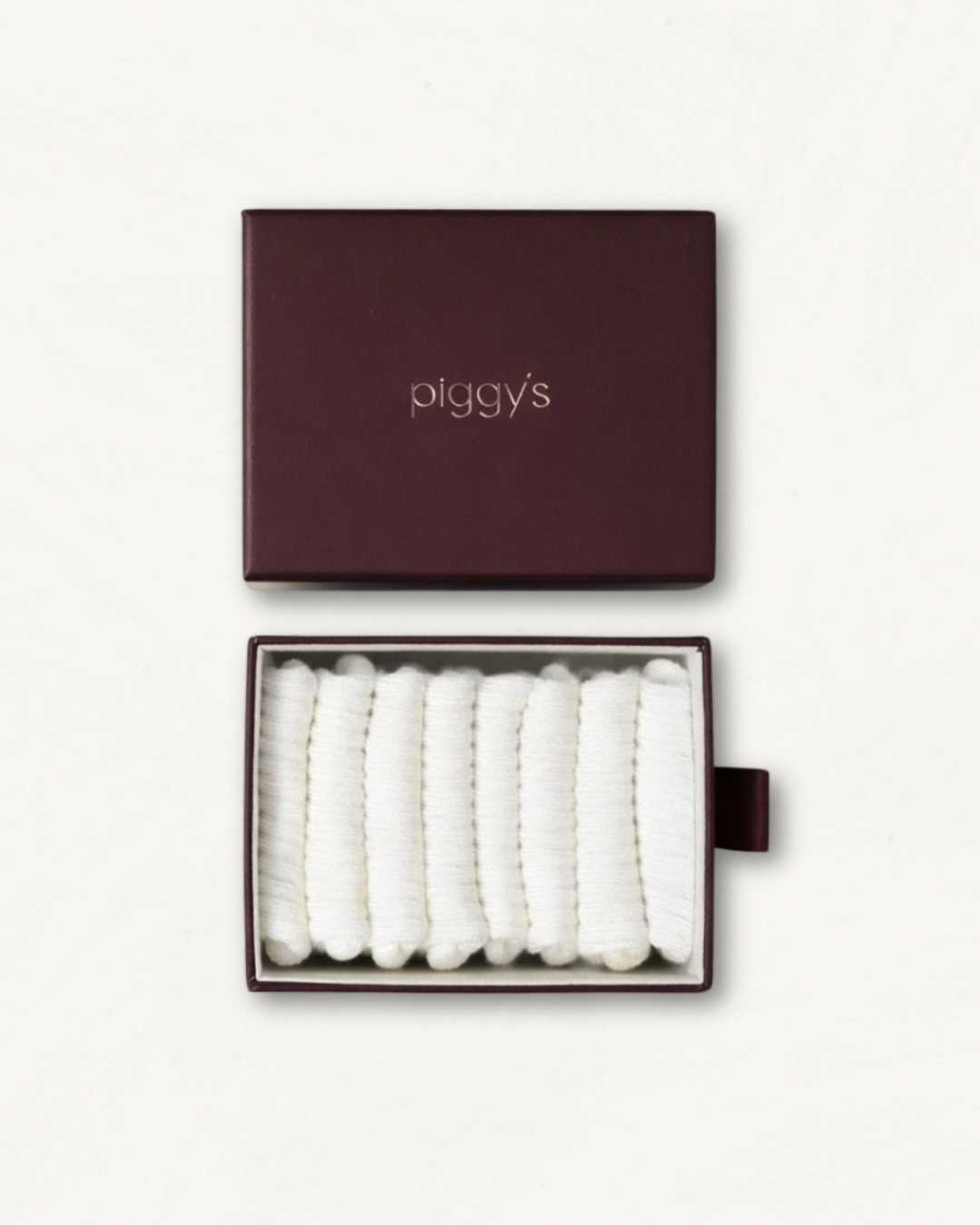 Open box displaying 4 pairs of white baby socks with 'piggy's' branding on a white background.