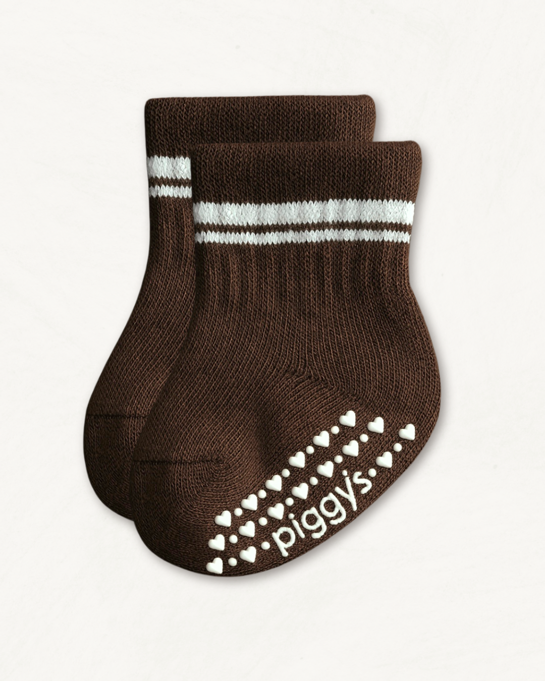 Pair of dark brown crew socks with white stripes and heart pattern silicone grips on an off-white background