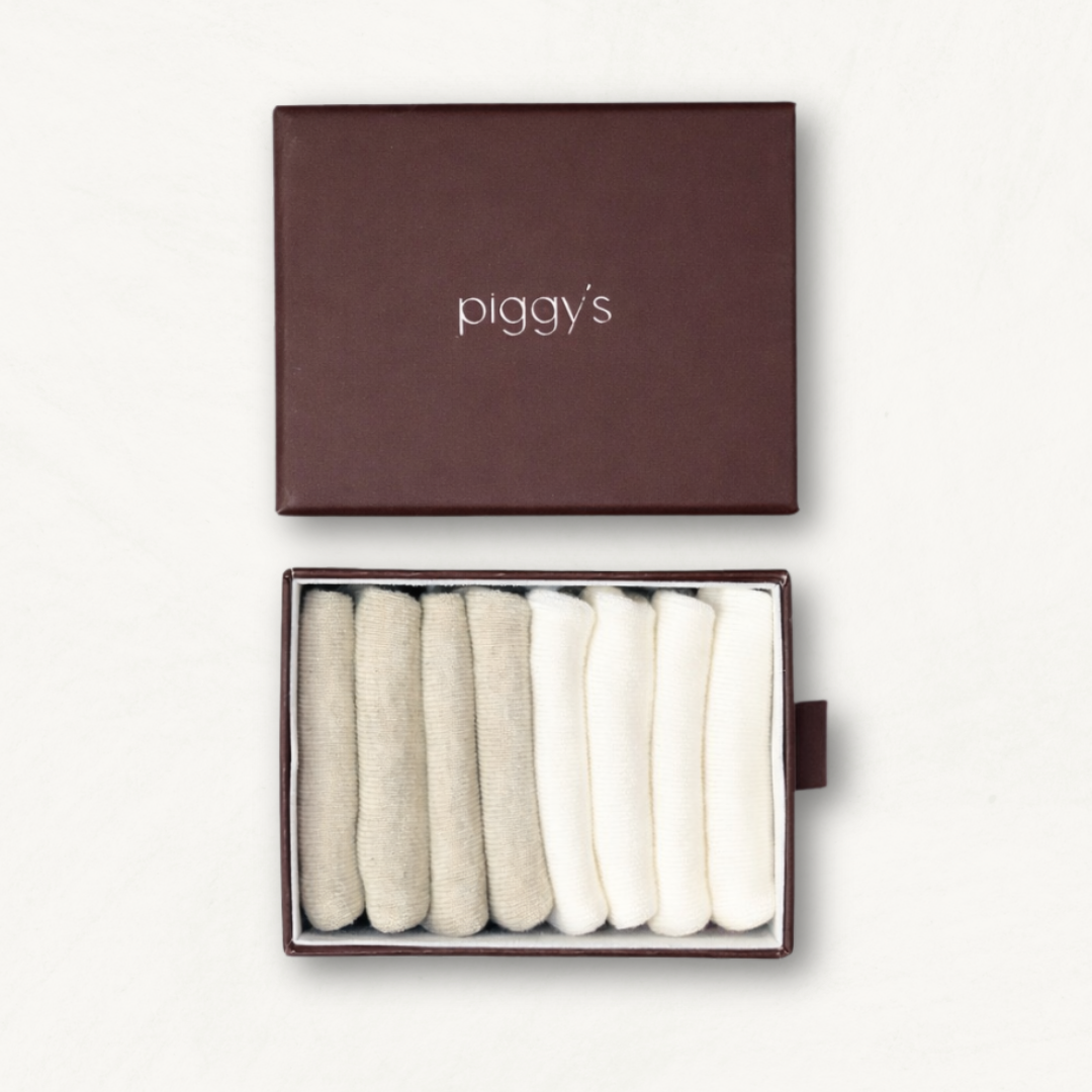 Open box displaying 2 pairs of heather beige and 2 pairs of white toddler socks with 'piggy's' branding on a white background.