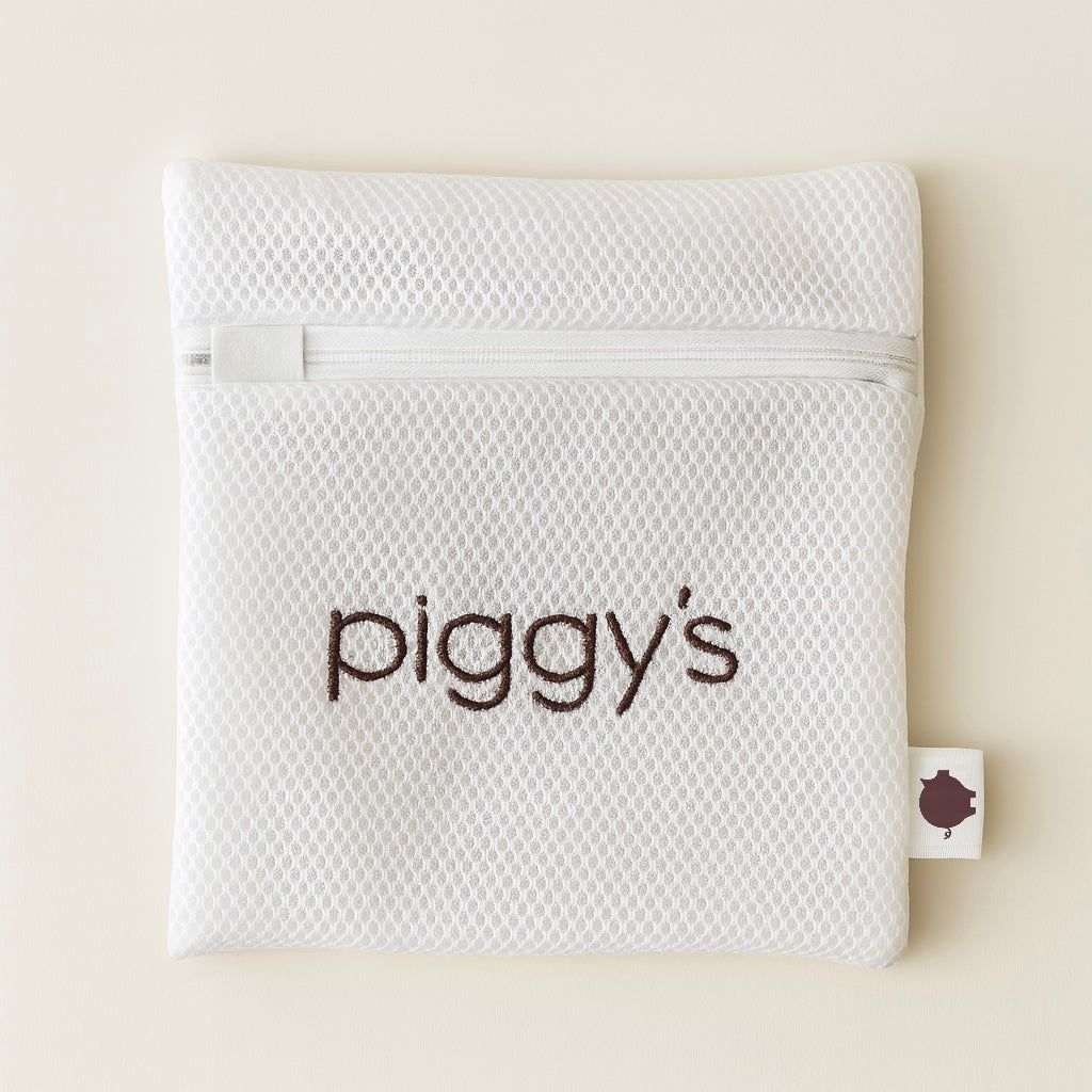 White mesh laundry pouch with zipper closure and 'piggy's' branding on a beige background