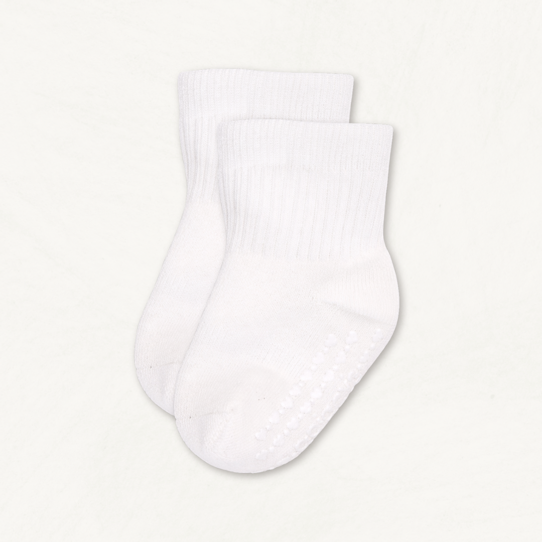 Pair of white baby crew socks with heart pattern silicone grips on an off-white background