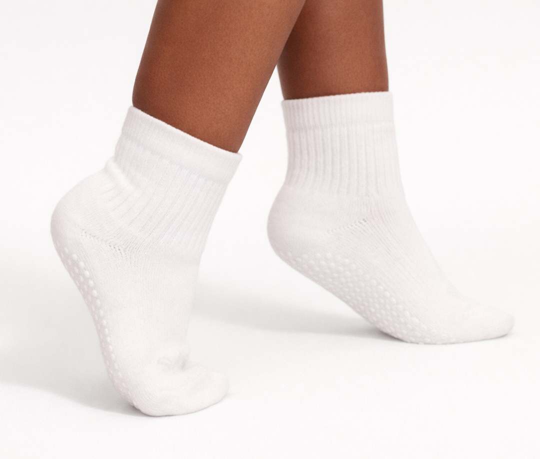 Pair of white toddler crew socks with silicone grips on an off-white background