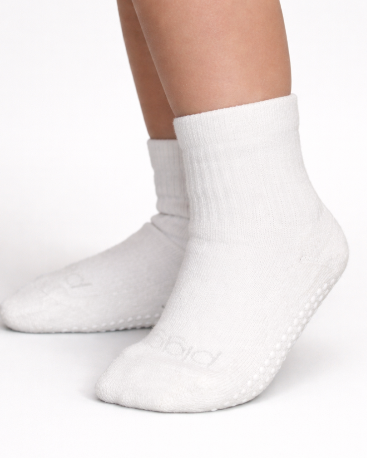 Pair of white toddler crew socks with silicone grips on an off-white background