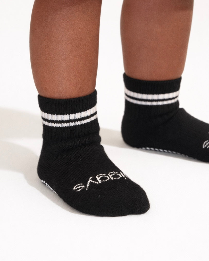 Pair of black toddler crew socks with silicone grips on an off-white background