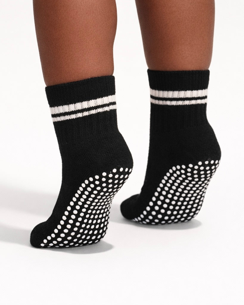 Pair of black toddler crew socks with silicone grips on an off-white background