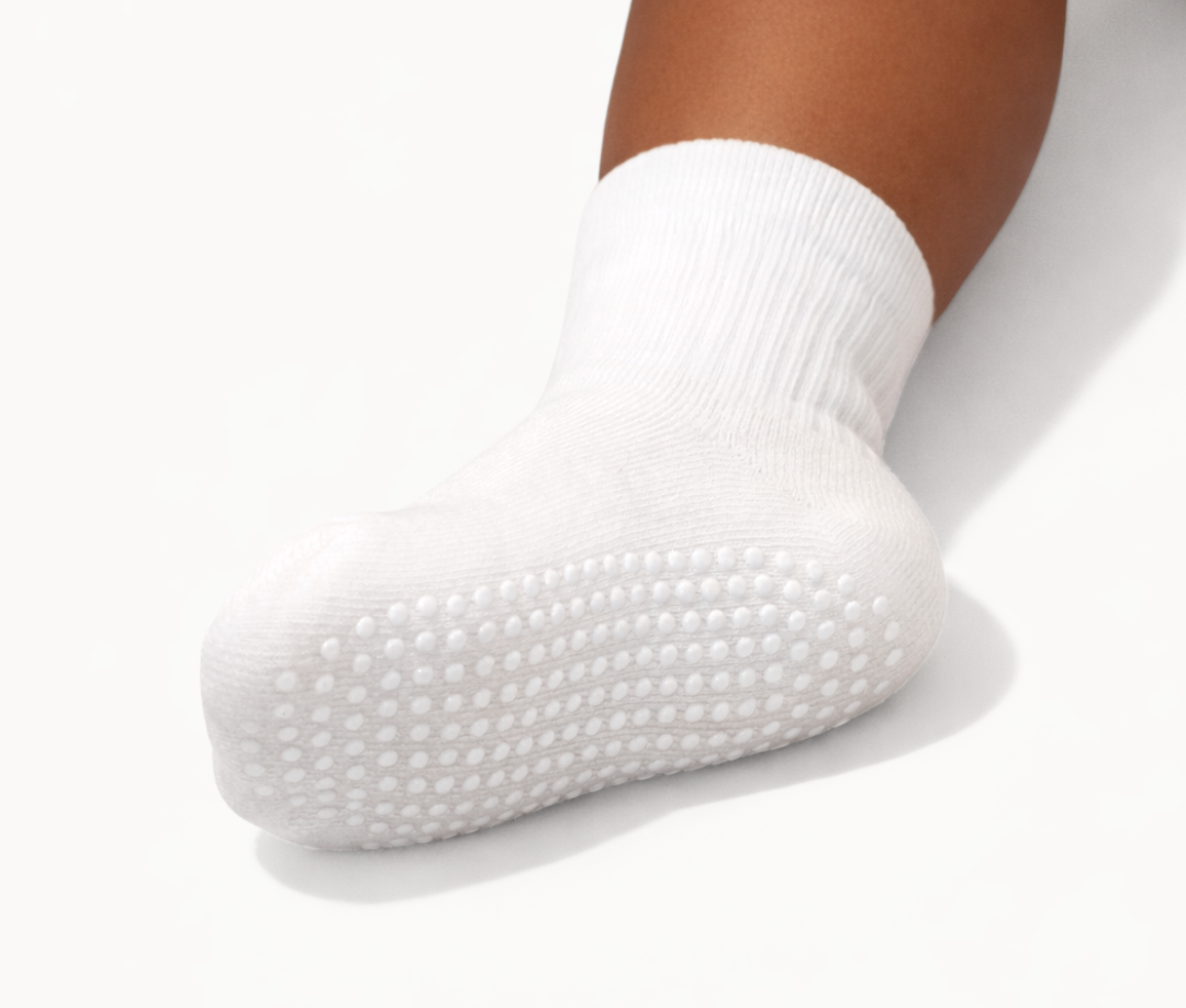 Single white toddler crew sock with white dot silicone grips on an off-white background