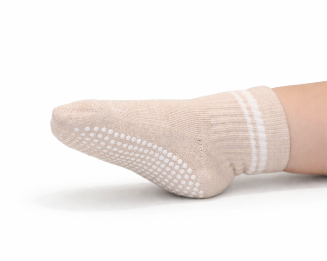 Single heathered beige toddler crew sock with white dot silicone grips on an off-white background