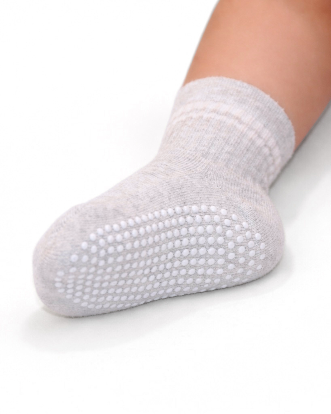 Single light heather grey toddler crew sock with white dot silicone grips on an off-white background