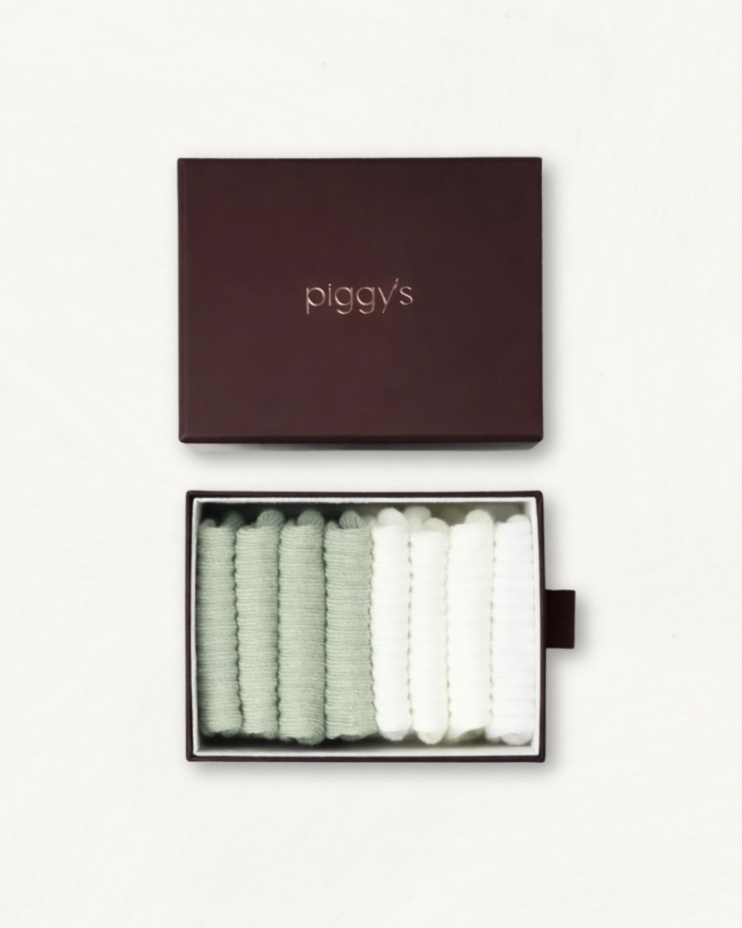 Open box displaying 2 pairs of sage and 2 pairs of white baby socks with 'piggy's' branding on a white background.
